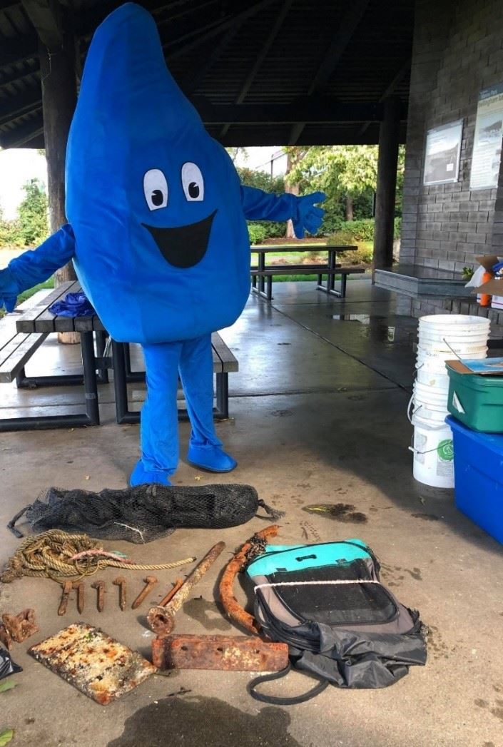 A cartoon water drop costume behind pieces of metal, rope, and netting